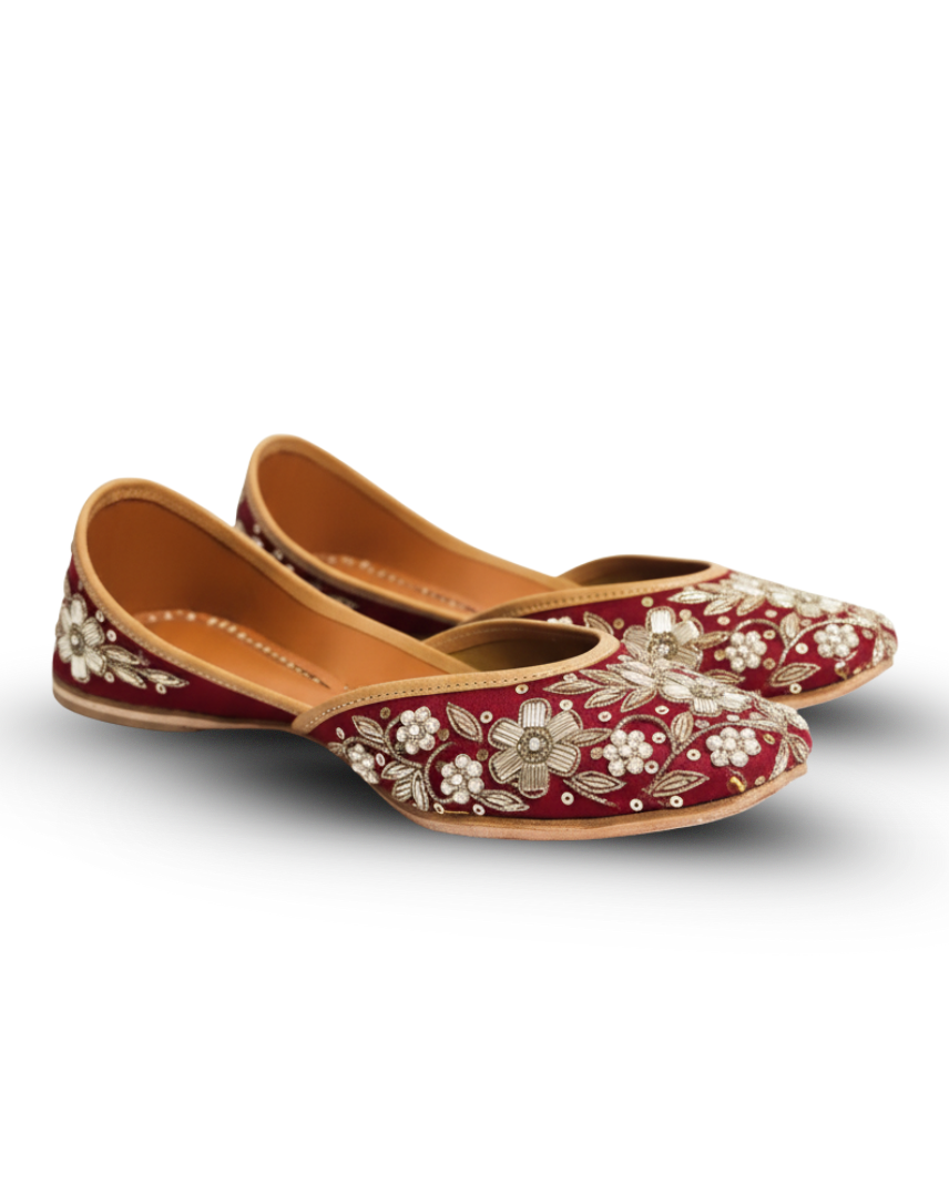 Pair of red juttis with gold floral embroidery on a white background
