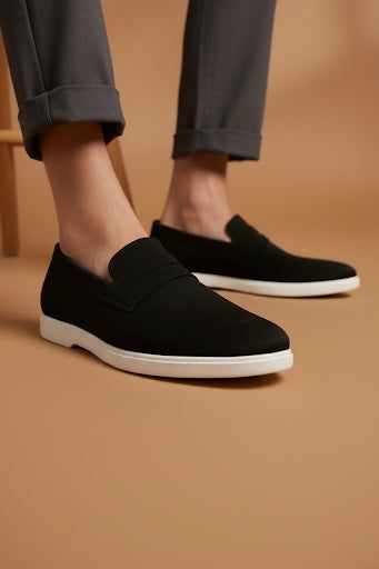 Black loafers with white soles worn by a person on a beige background