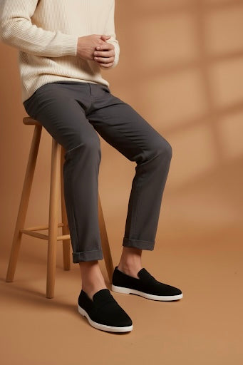 Person wearing dark gray pants and black slip-on shoes against a brown background