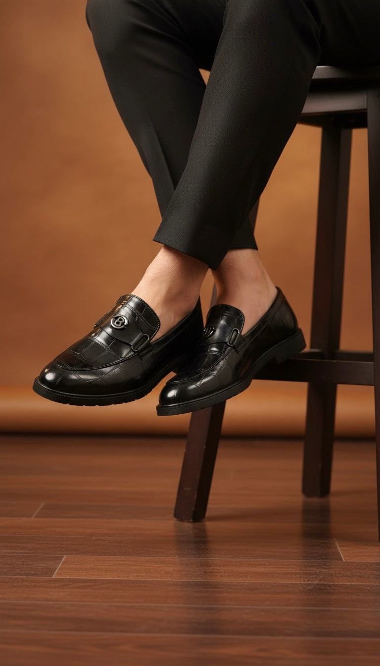 Person wearing black dress shoes and pants sitting on a wooden stool with a brown background