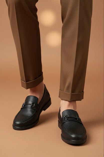 Black loafers worn with brown pants on a beige background