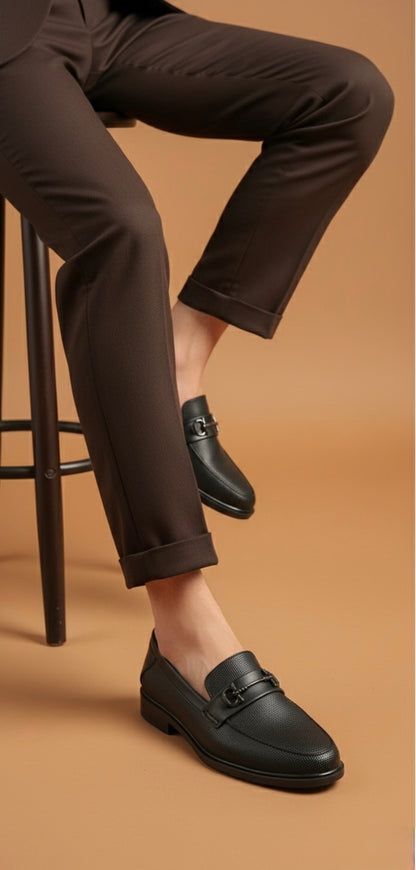 Person wearing black loafers and dark brown pants on a brown background