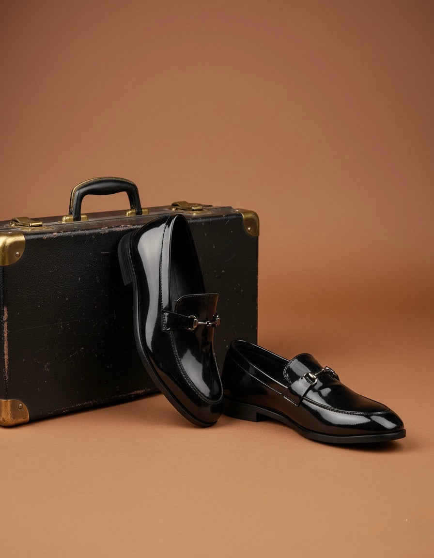 Black patent leather shoes and vintage suitcase on a brown background