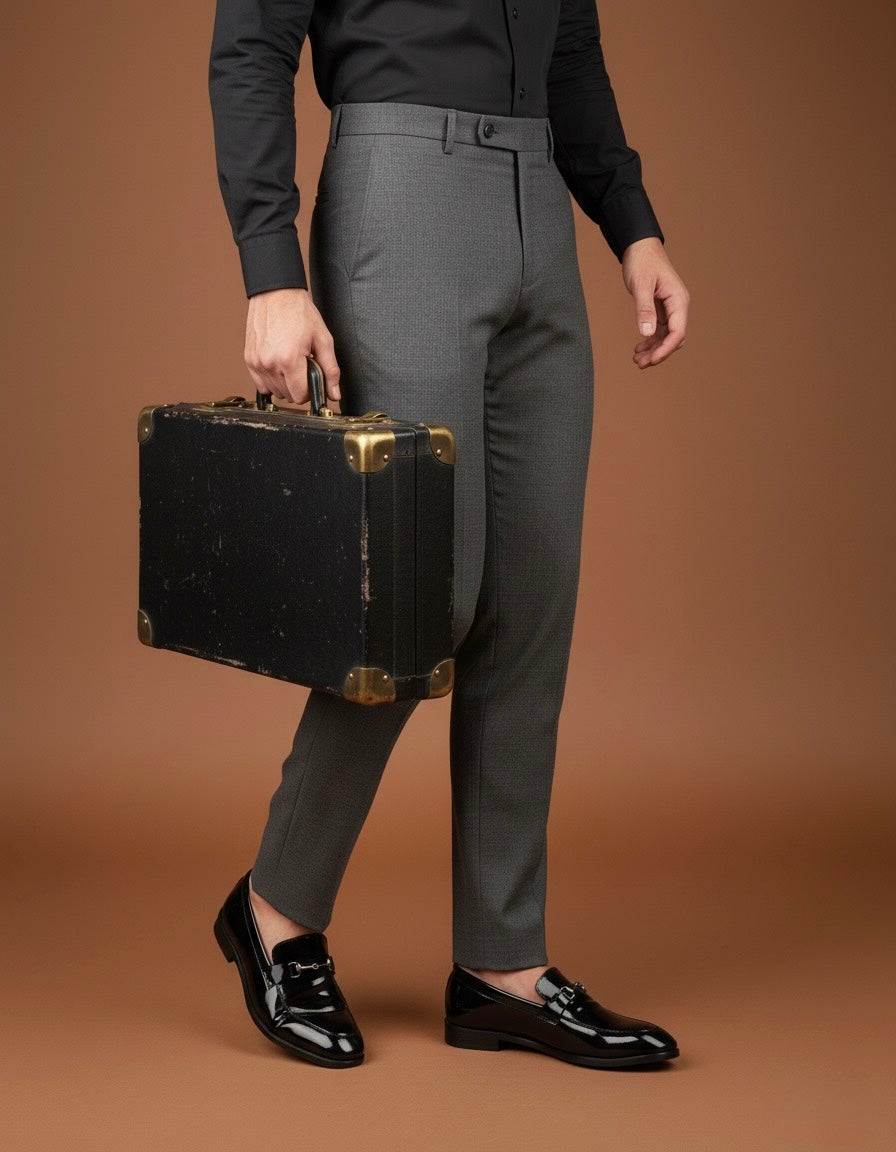 Person holding a vintage suitcase wearing gray pants and black shoes on a brown background