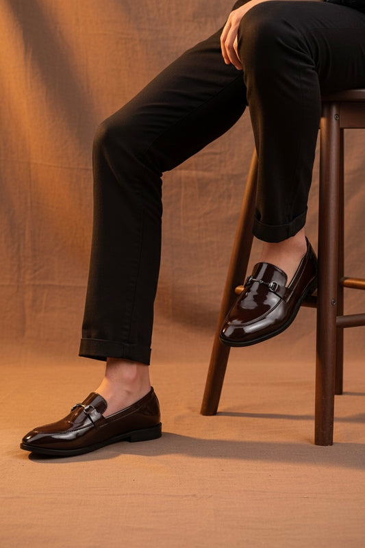 Person wearing black dress shoes and black pants sitting on a wooden stool against a brown background