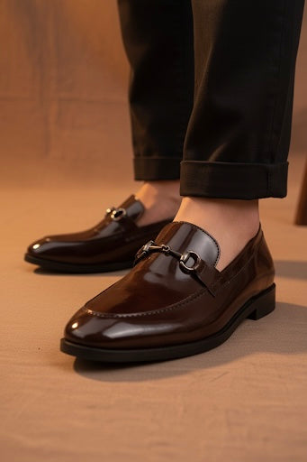 Brown leather loafers worn with black pants on a wooden floor.