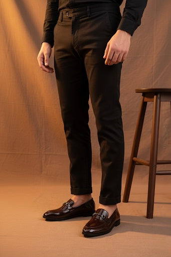 Person wearing dark brown pants and shoes against a brown background
