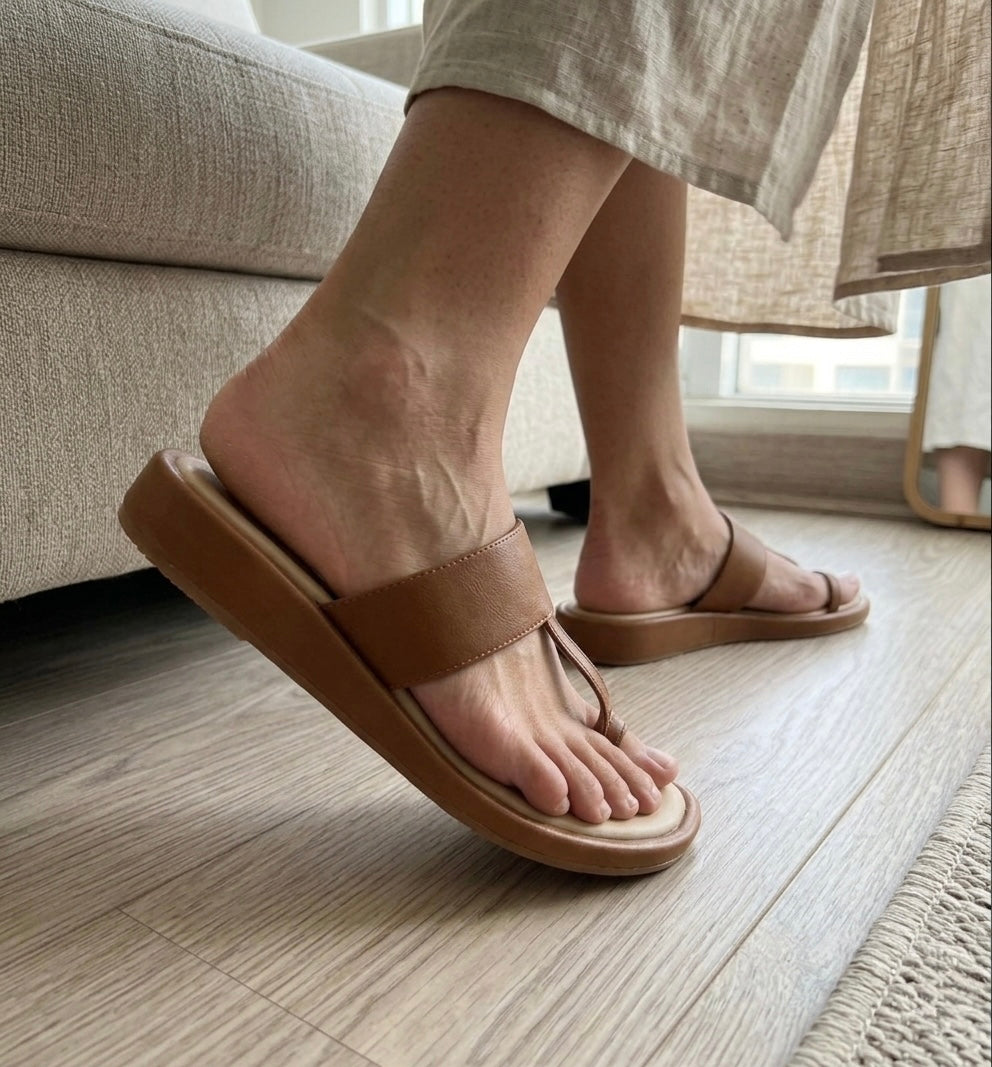 Person wearing brown flt kolhapuri sliders sandals on a wooden floor.