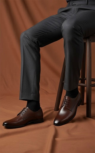 Person wearing dark gray pants and brown dress shoes on a brown background