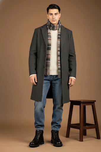 Man wearing a gray coat, patterned scarf, and jeans standing against a brown background