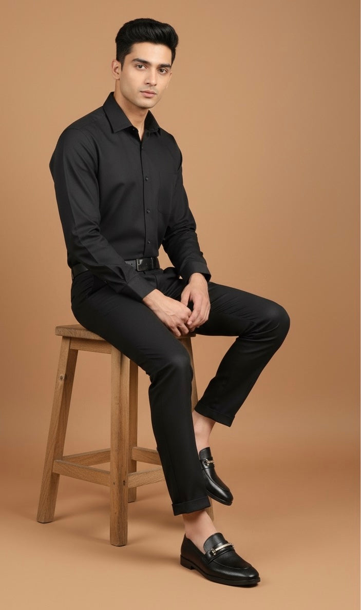 Man wearing a black shirt and pants sitting on a wooden stool against a brown background
