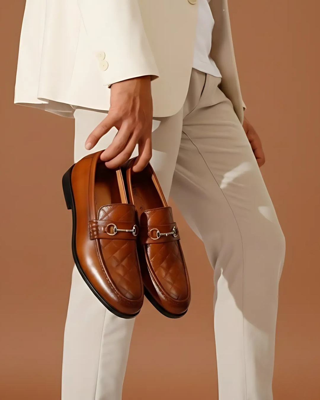 Person holding a pair of brown loafers against a beige background
