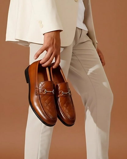 Person holding a pair of brown loafers against a beige background