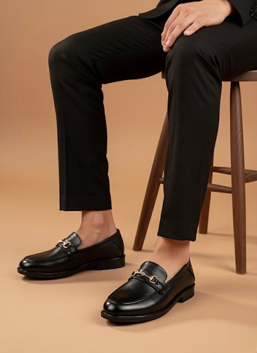 Person wearing black dress shoes with gold buckles on a beige background