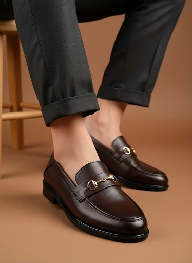 Brown loafers with gold buckles worn by a person on a brown background
