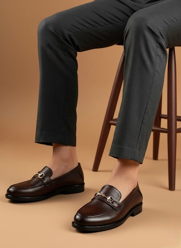 Brown leather loafers worn with dark pants on a beige background