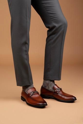 Brown dress shoes with a person wearing gray pants and socks on a beige background