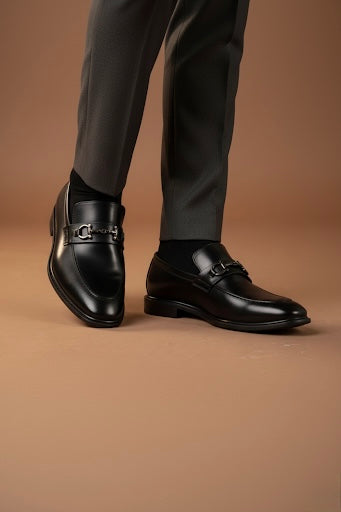Black dress shoes worn with gray pants on a brown background