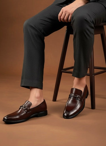 Brown leather loafers worn with dark trousers on a brown background