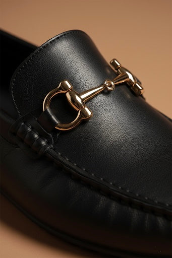 Black loafer with gold buckle on a beige background