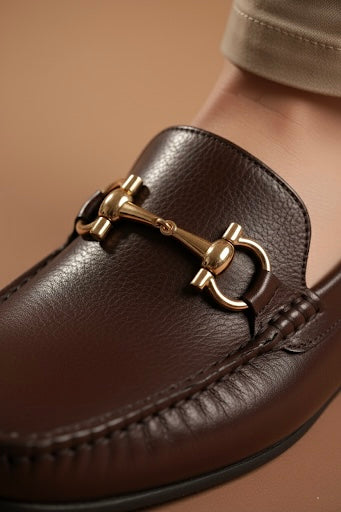 Brown leather loafer with gold buckle on a beige background